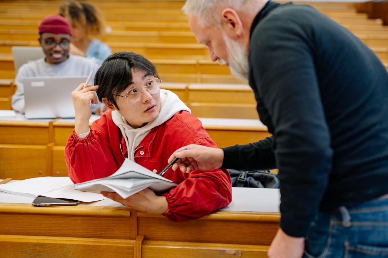 A professor assisting a college student during class in a university lecture hall.